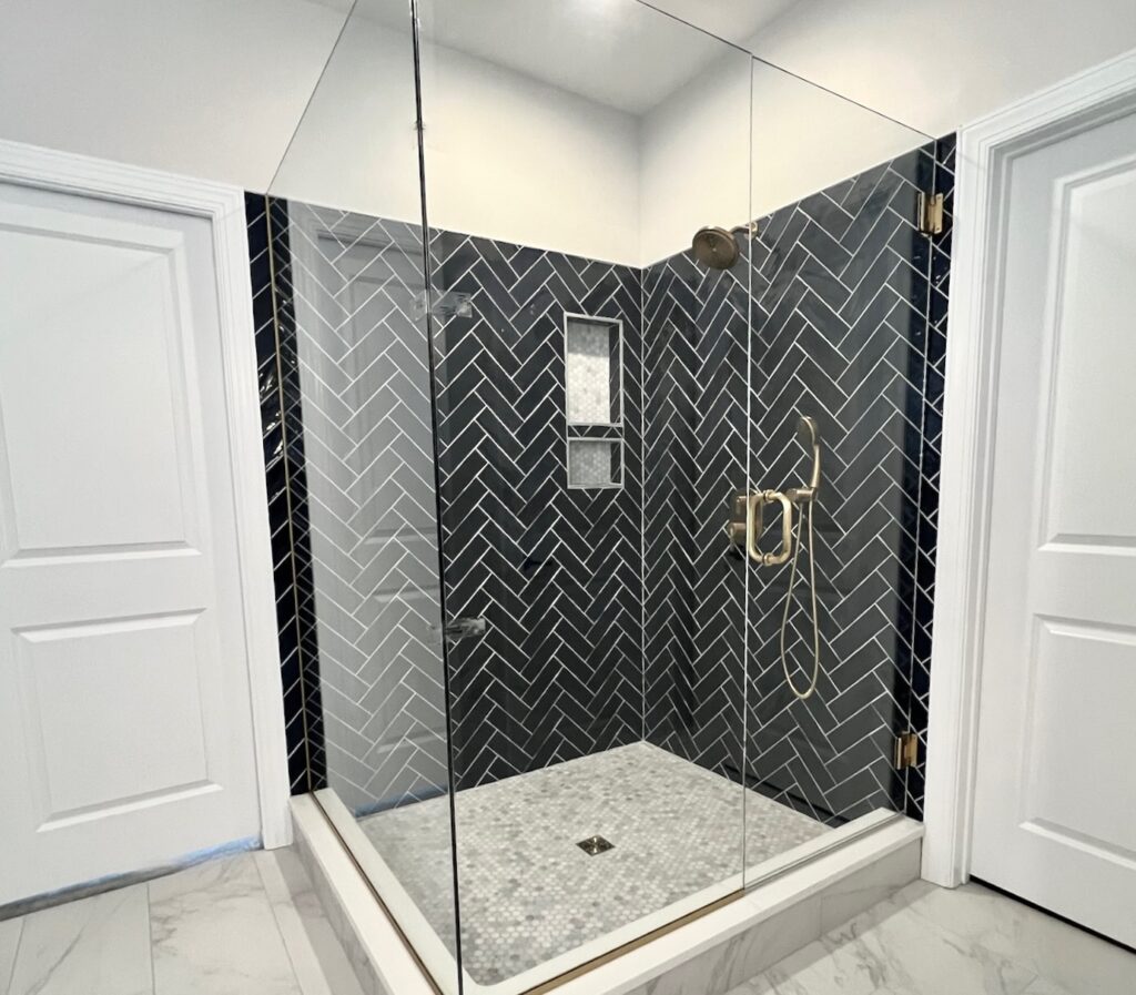 After: herringbone tile shower with frameless glass surround