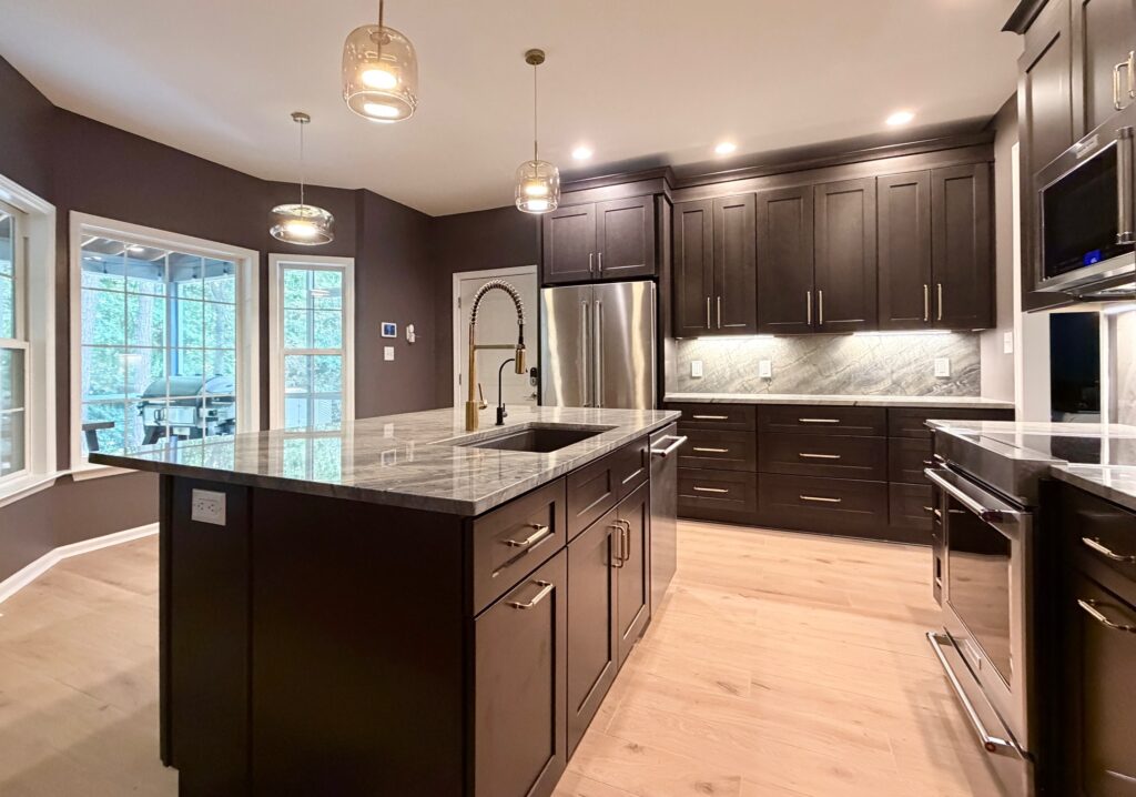 Newly remodeled kitchen with dark shaker cabinets, gray Moreno quartzite countertops, a large island, stainless steel appliances, and modern pendant lighting.