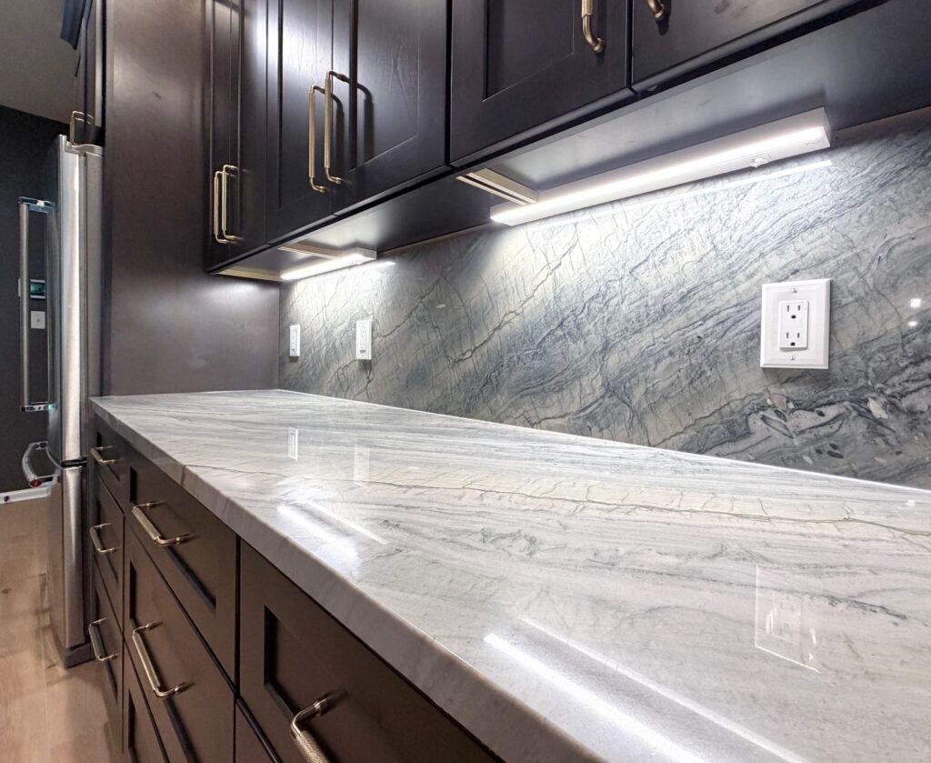 Newly remodeled kitchen with dark shaker cabinets, gray Moreno quartzite countertops, a large island, stainless steel appliances, and modern pendant lighting.