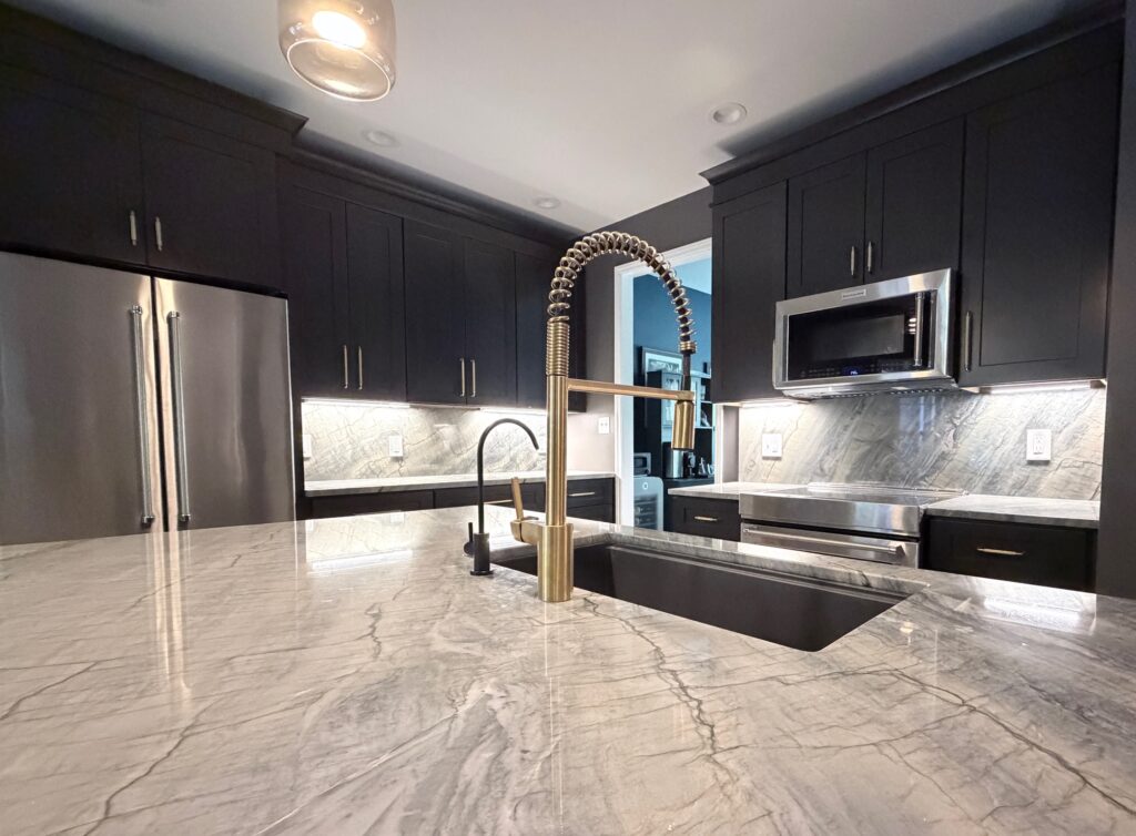 Newly remodeled kitchen with dark shaker cabinets, gray Moreno quartzite countertops, a large island, stainless steel appliances, and modern pendant lighting.